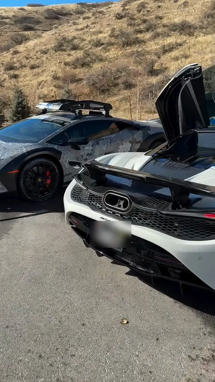 A white McLaren with its door raised beside a hex-camo-wrapped Lamborghini