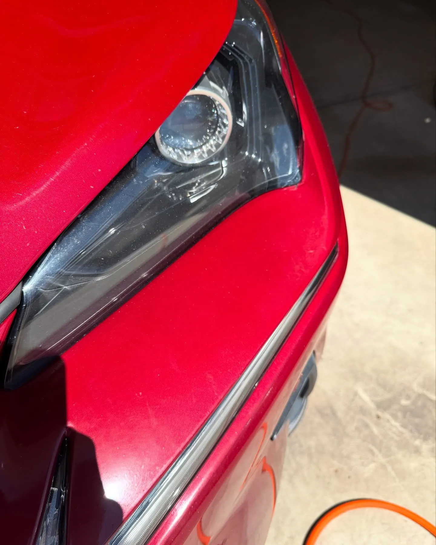 The headlight and fender of a red Lexus NX, metallic flake visible in the paint