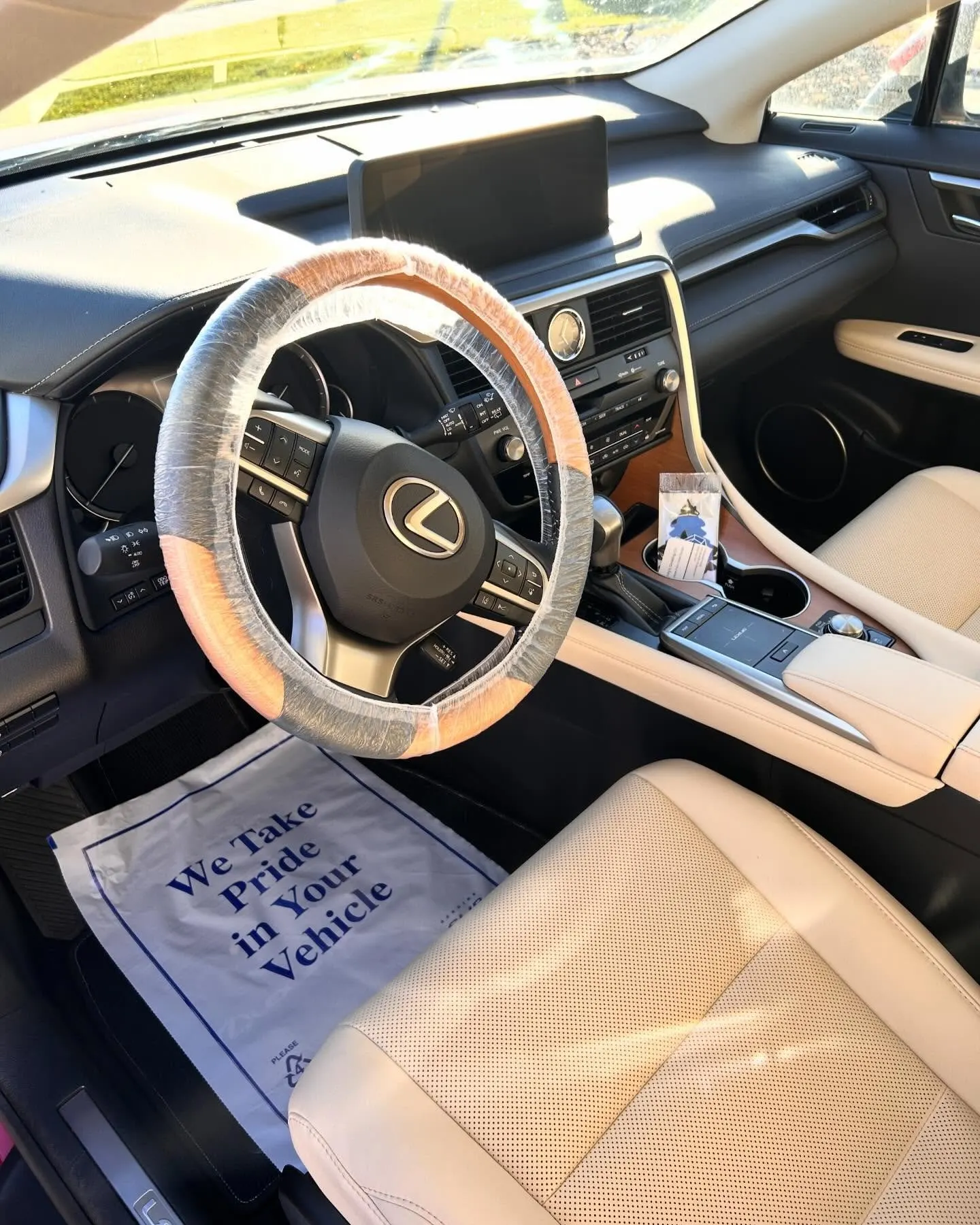 The tan leather cockpit of a Lexus RX, wrapped steering wheel and a care card on the seat