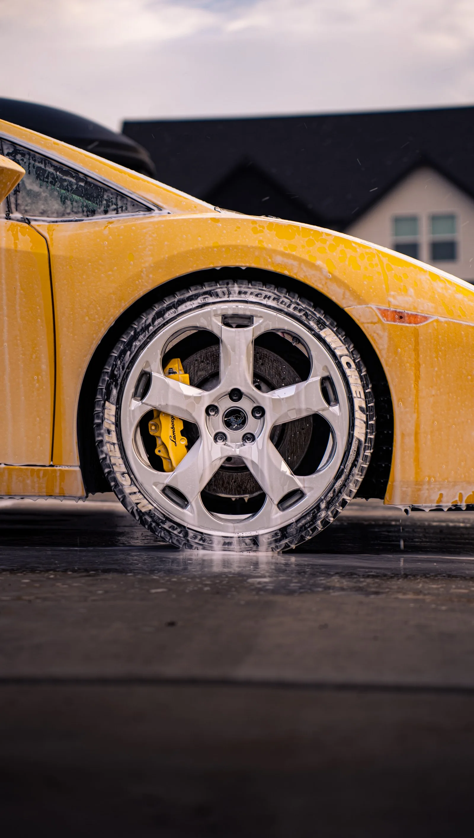 A detailer scrubbing the sudsy wheel of a yellow Lamborghini Gallardo with a dedicated brush