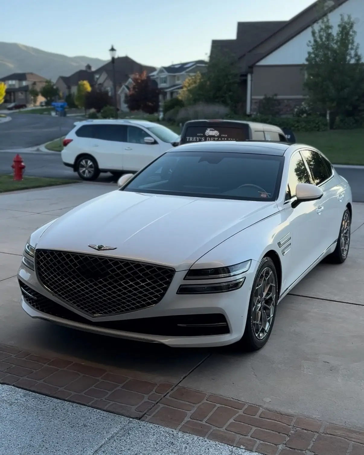 A white Genesis G80 in a driveway at dusk