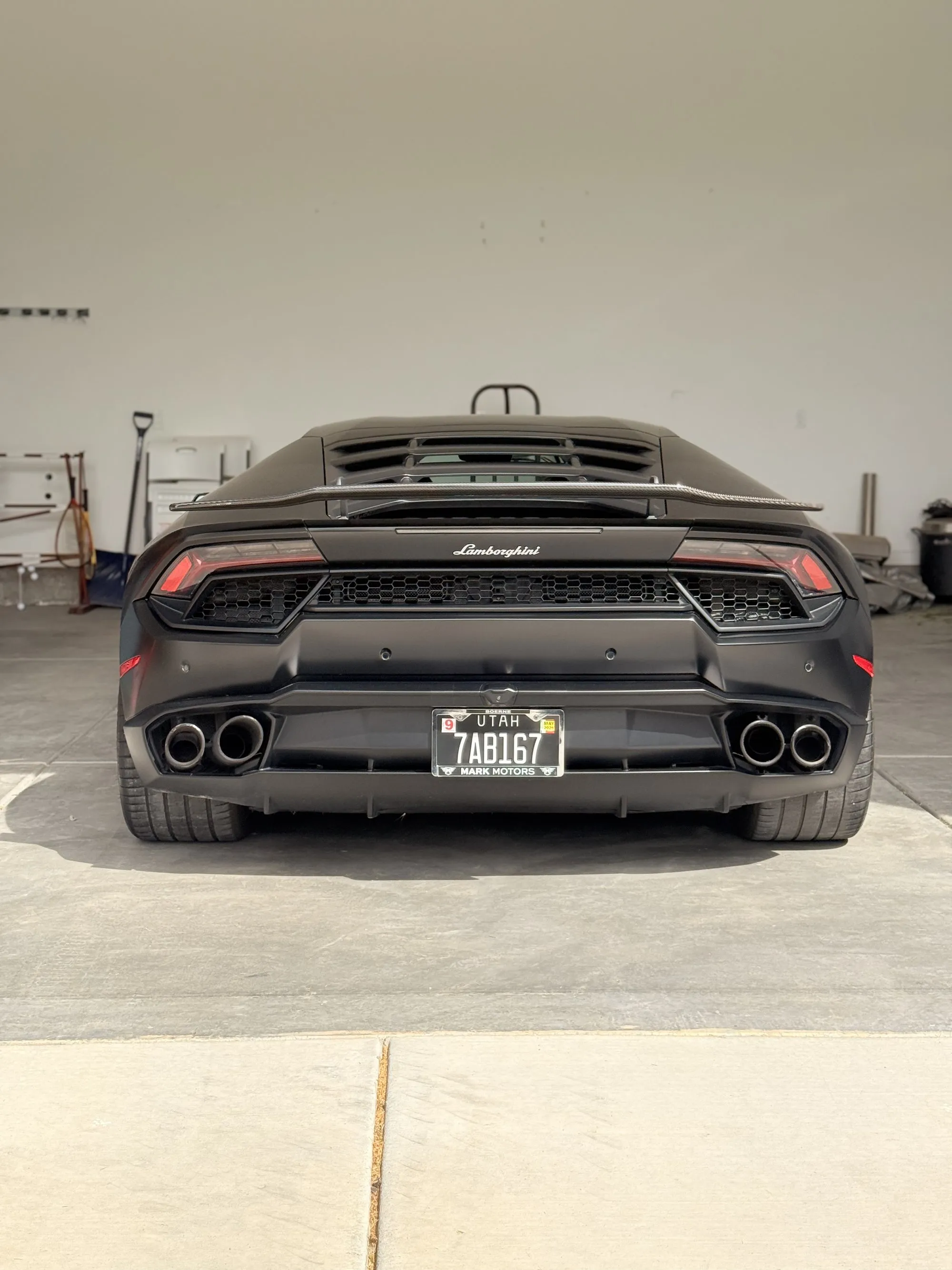A matte black Lamborghini Huracan from the rear, full car in the garage