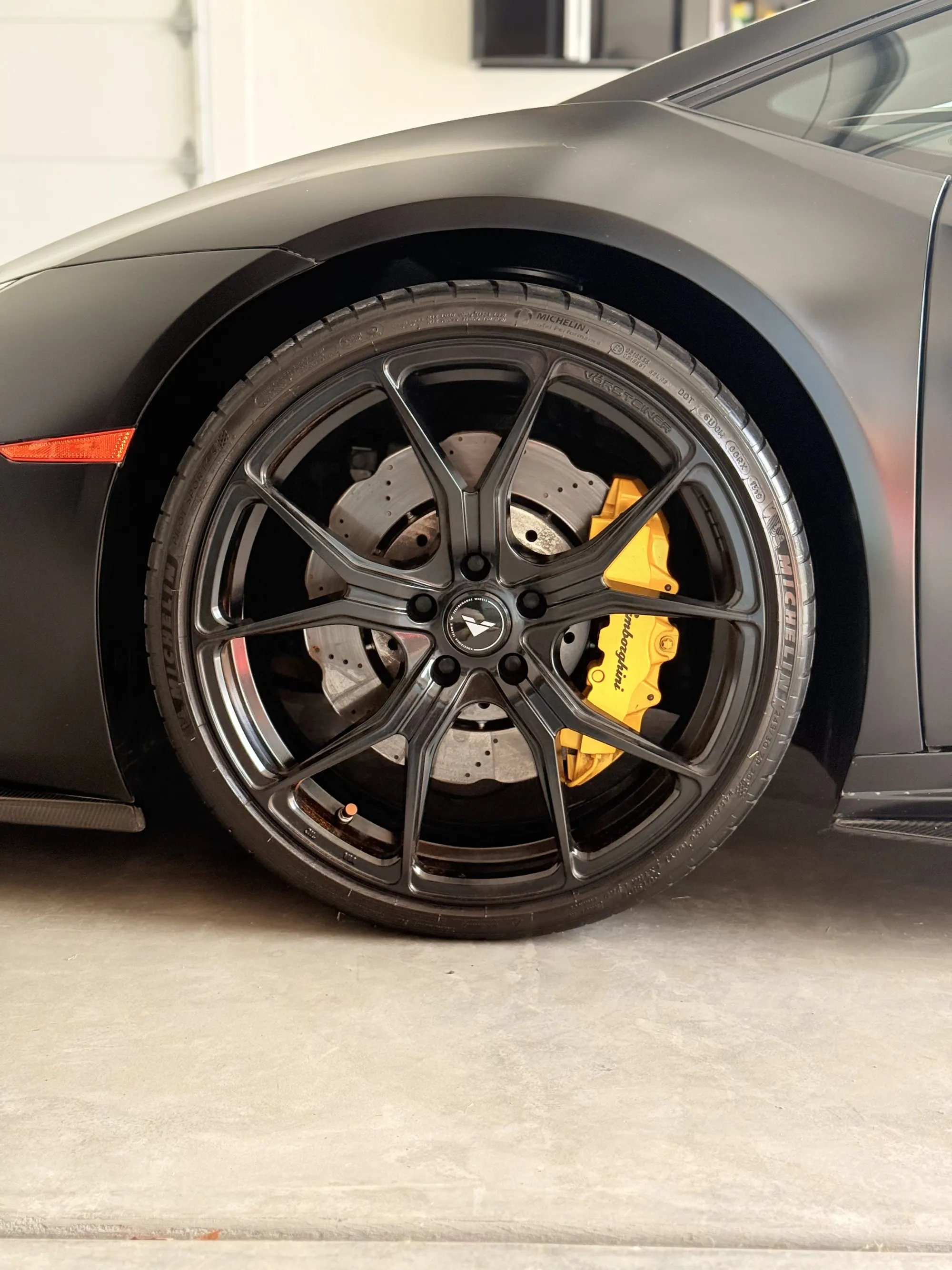 The front wheel of a matte Lamborghini Huracan with a yellow brake caliper, up close
