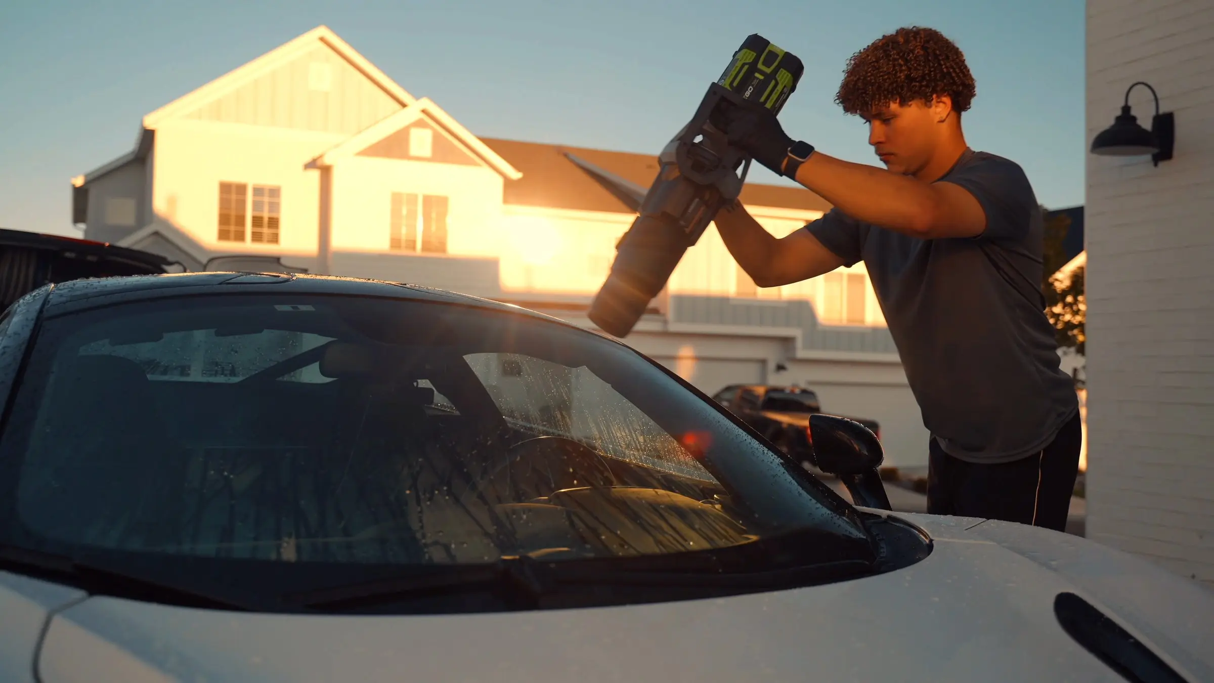 A detailer blow-drying the windshield of a white McLaren 720S at sunset