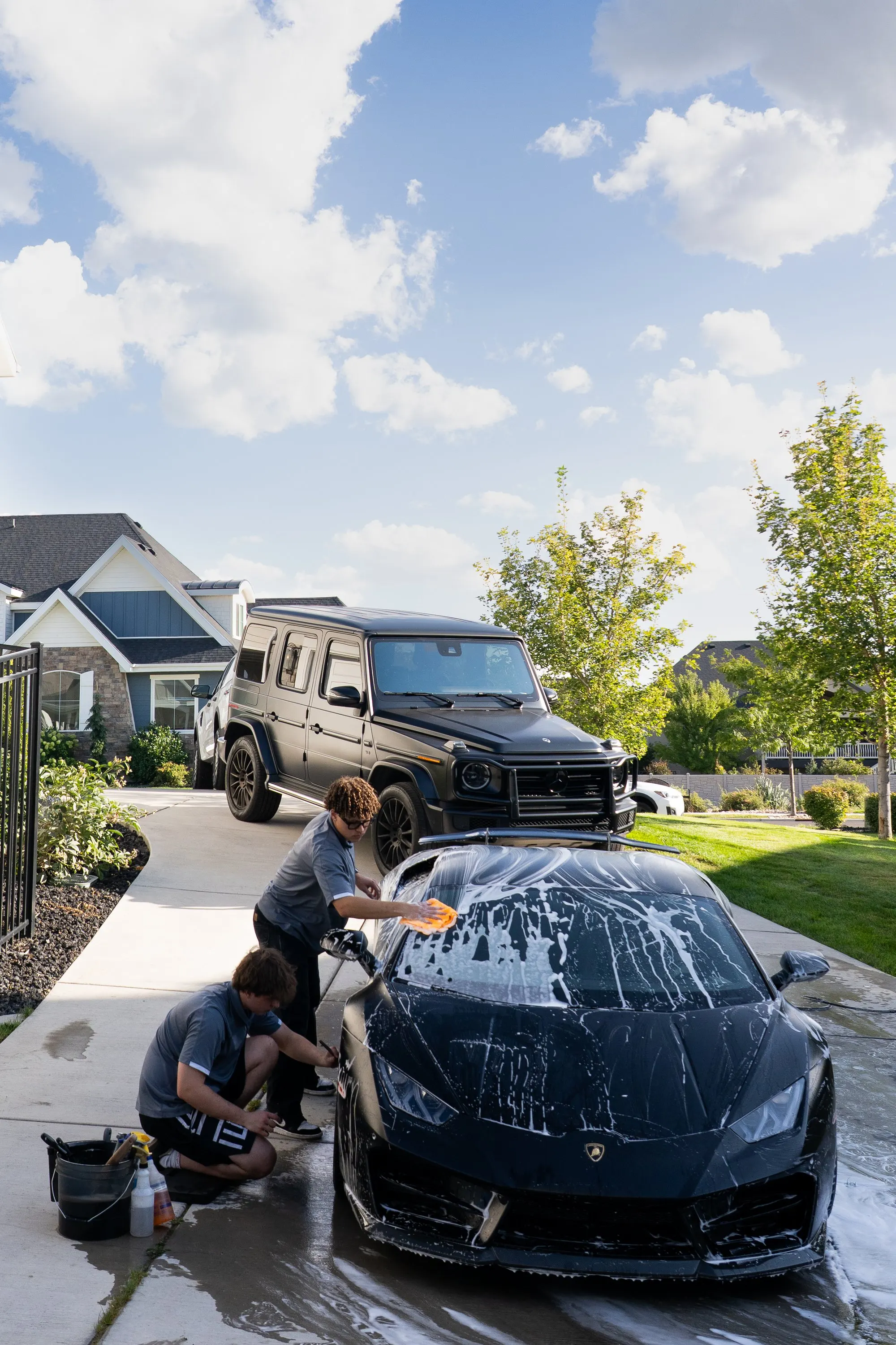 A technician washing a sudsy black Lamborghini Huracan low at the rocker